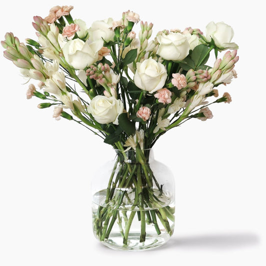 A bouquet of white and pale pink flowers arranged in a clear glass vase with water, photographed against a clean white background.